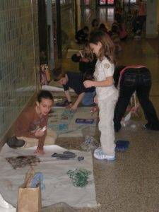 A group of kids paints on the floor of a hallway