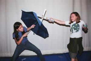 Two kids doing a sword fight with an umbrella