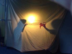 Two people act out behind a sheet with a flashlight